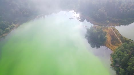 Aerial-top-down-shot-of-exotic-lake-lighting-by-sun-surrounded-by-deep-forest-scenery-in-Indonesia