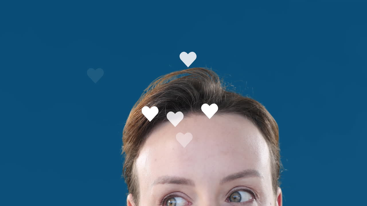Animation of heart shapes flying over caucasian young woman raising eyebrows over blue background