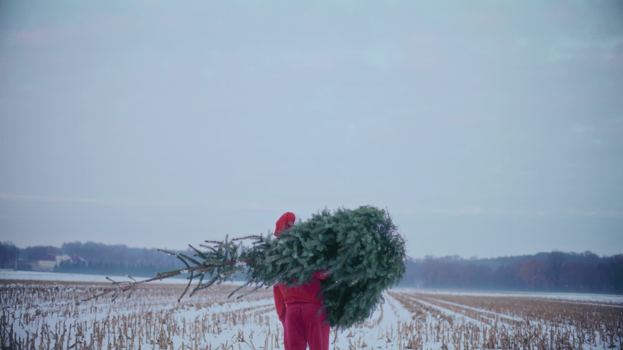 Mand med nissehue, der bærer juletræ på skulderen om vinteren