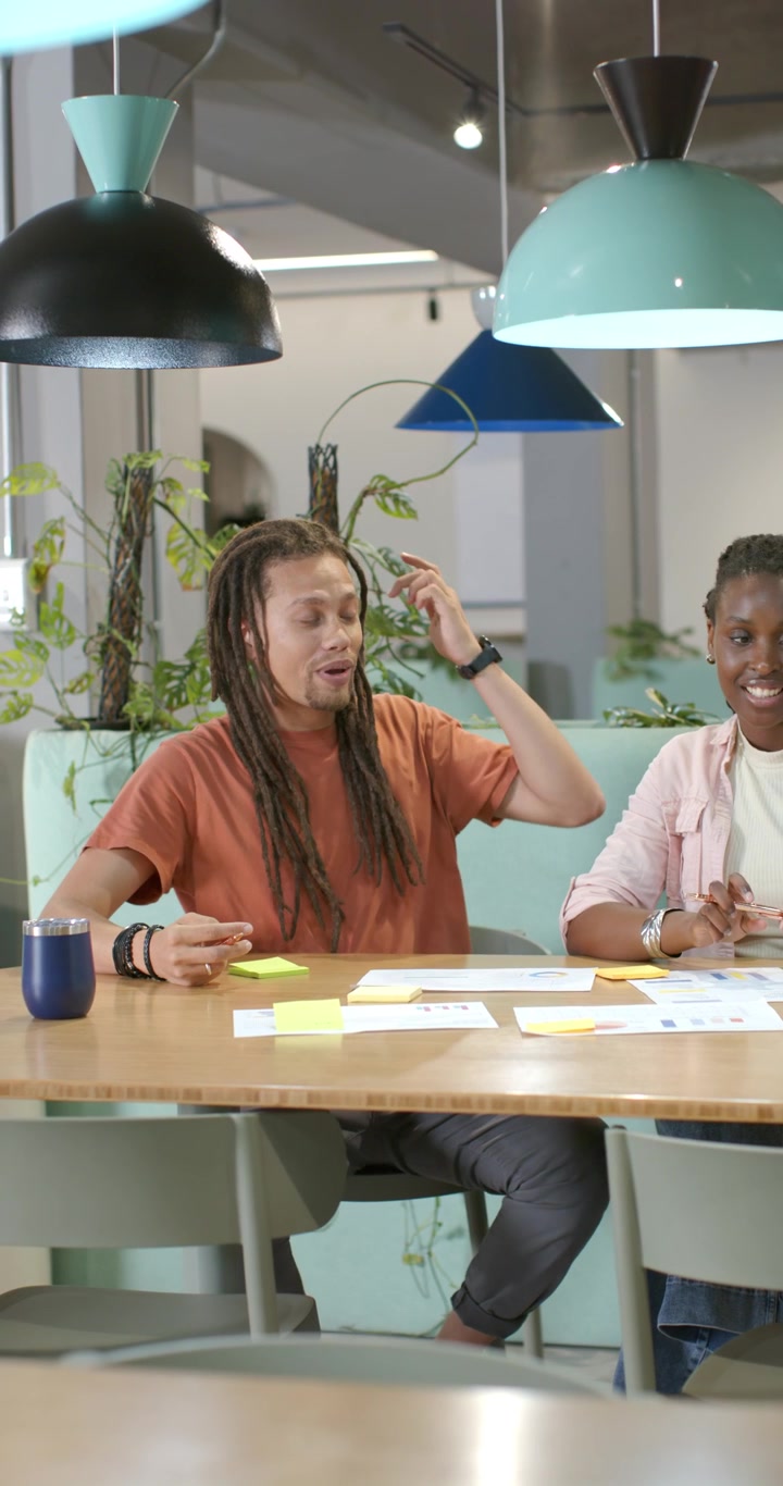 Vertical video: African American coworkers reviewing sticky notes and laptop in lounge, finalizing