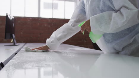 midsection of cleaner wearing protective overalls disinfecting office and furniture