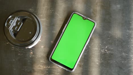 teléfono inteligente con pantalla verde y taza de café en una mesa