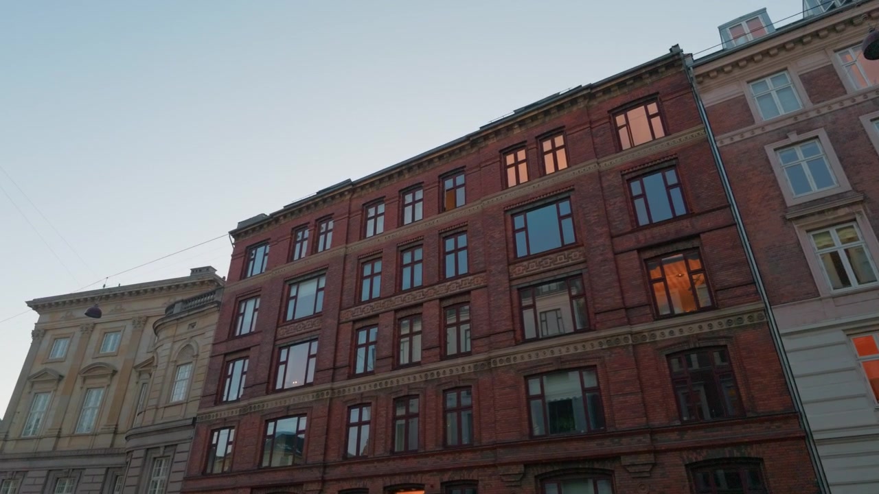 Strada con facciate di edifici in mattoni al tramonto, ripresa con stabilizzatore gimbal. Vista in tracking a 60fps che guarda in alto un blocco architettonico bianco e rosso a Copenaghen, Danimarca