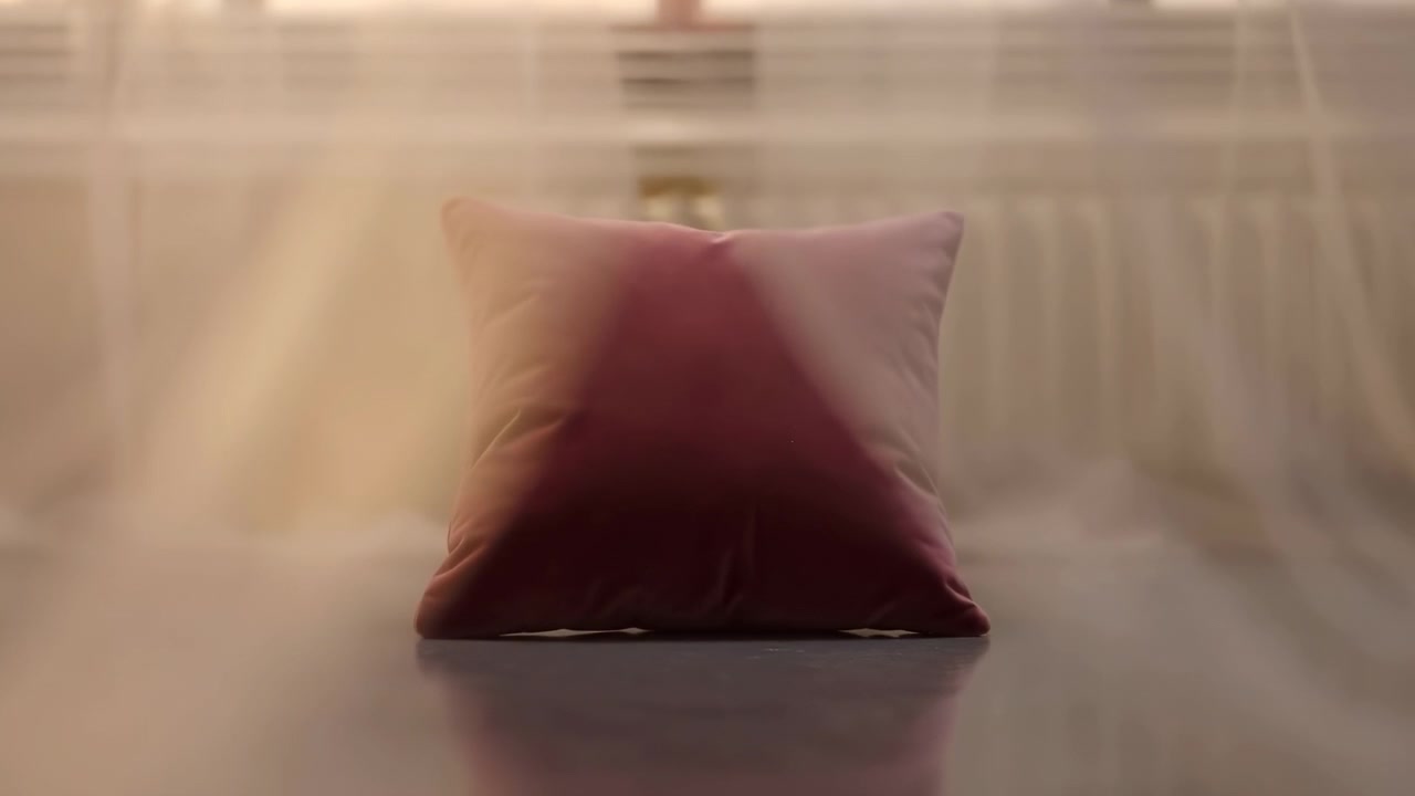 Primo piano centrato che mostra un cuscino bordeaux rivelato mentre le tende velate si aprono ai lati; tessuto traslucido con pieghe delicate e trama fine incornicia il cuscino, atmosfera calda.