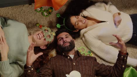 looking down on group of friends lying on floor dressing up with irish novelties and props at home for st patrick's day party