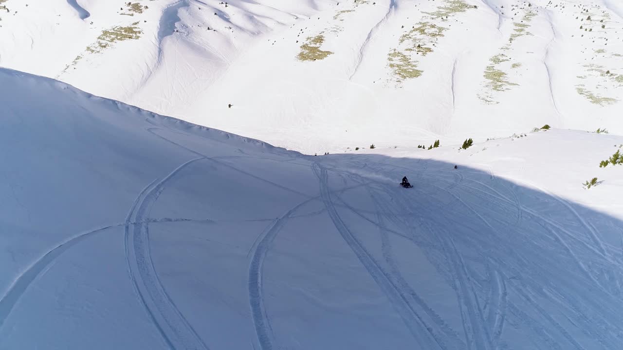 vista escénica de una moto de nieve rápida que se acerca a un dron en una montaña nevada blanca con líneas de seguimiento de máquina de nieve en la sombra en un día soleado, akoura, líbano, antena hacia atrás