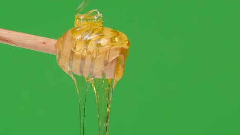 4k. fresh honey pouring and flowing from wooden dipper spoon on green background