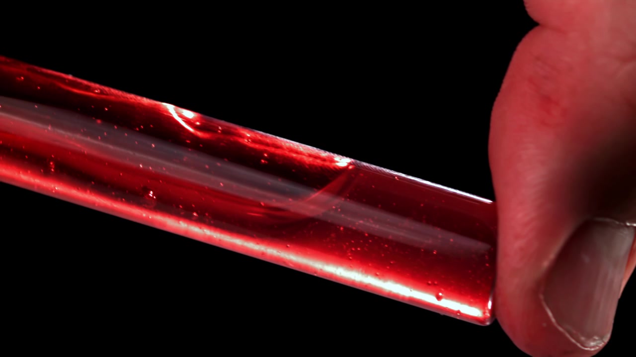 Nahaufnahme einer Hand, die ein Reagenzglas mit wirbelnder roter Flüssigkeit hält