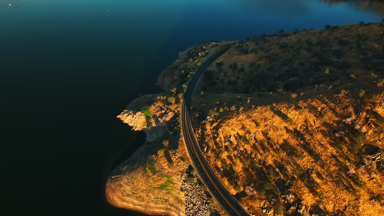 Highway going around the mountain in the picturesque scenery of California desert. Calm waters of lake around the rock. Top view.