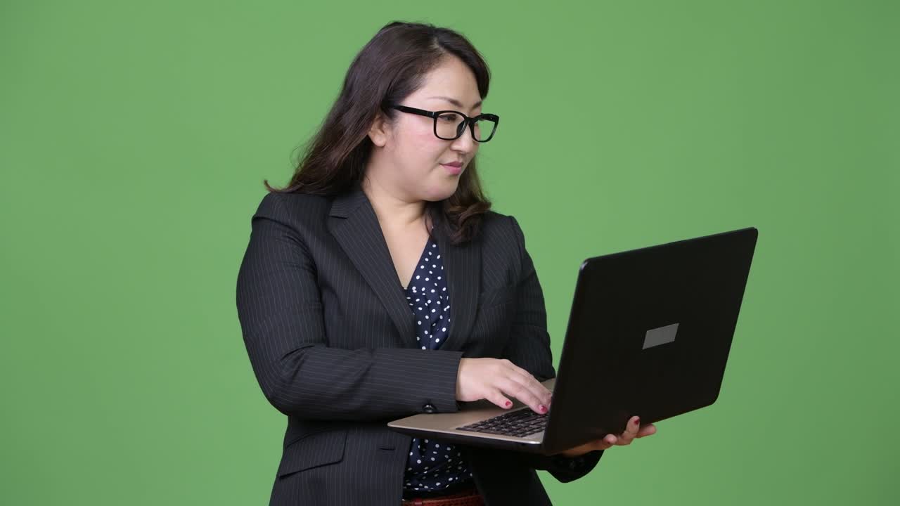 una hermosa mujer de negocios asiática madura usando una computadora portátil contra un fondo verde