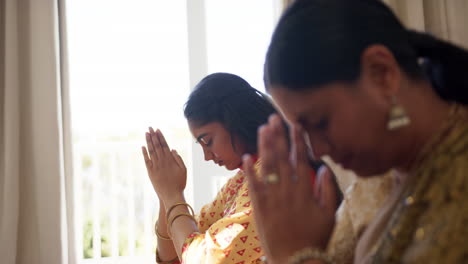 praying together, indian mother and daughter bowing heads and holding hands in traditional sari