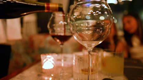 A wine bottle pours into a glass at a cozy, candlelit dinner setting with blurred background