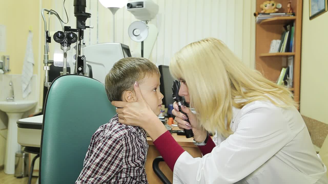 Side view of female pediatric optometrist examining eyes of little boy. Children ophthalmology