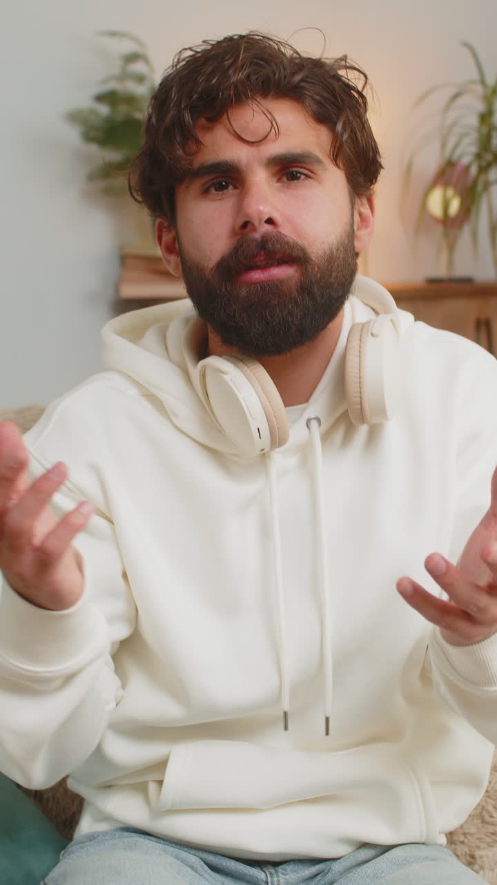 joven vlogger feliz sonriendo amigablemente a la cámara y agitando la mano mientras está sentado en el sofá en casa