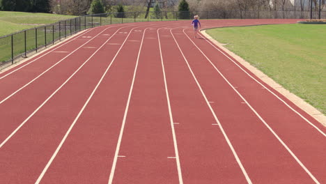 teen girl runs track towards camera in slow motion on a pretty day