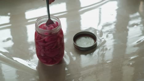 eating pickled red onion in glass jar using fork. high angle shot