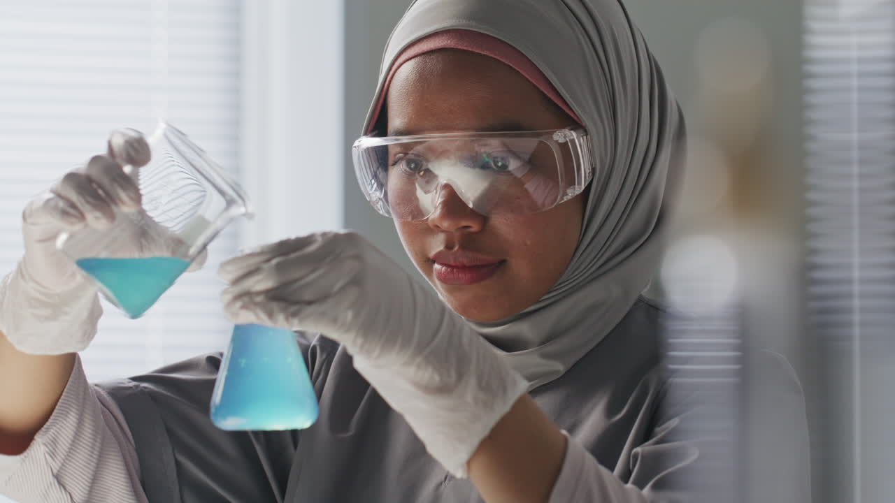 Kimiawan Wanita Berhijab Mengisi Labu dengan Cairan Biru di Laboratorium