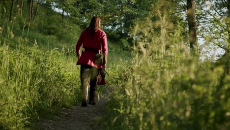Low-angle-view-of-a-man-wearing-traditional-medieval-costume-walking-through-the-woods