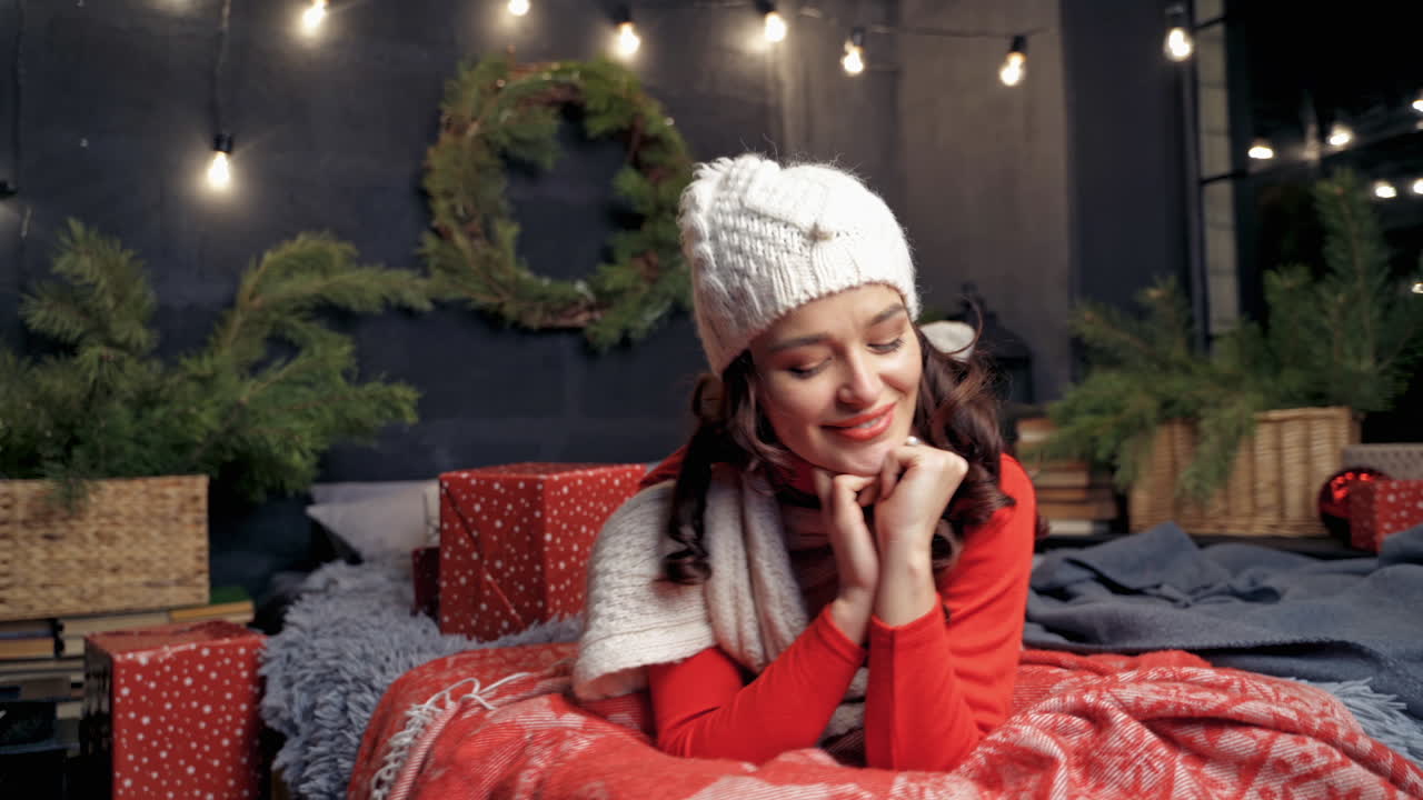 Portrait of a beautiful woman on bed. Smiling young female having fun at home on Christmas tree background. Positive girl looking at camera at New year.
