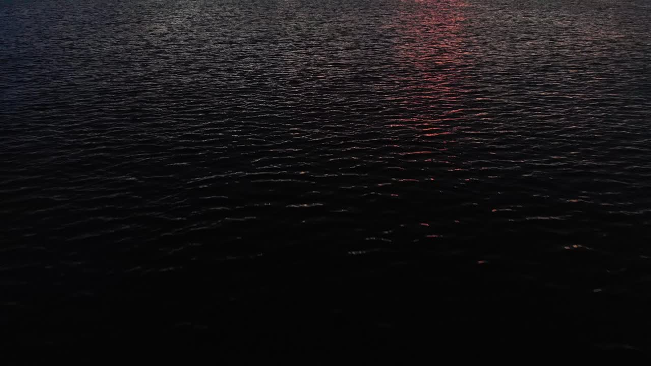 volando sobre un océano en calma, inclinándose hacia arriba y revelando islas y un amanecer nublado