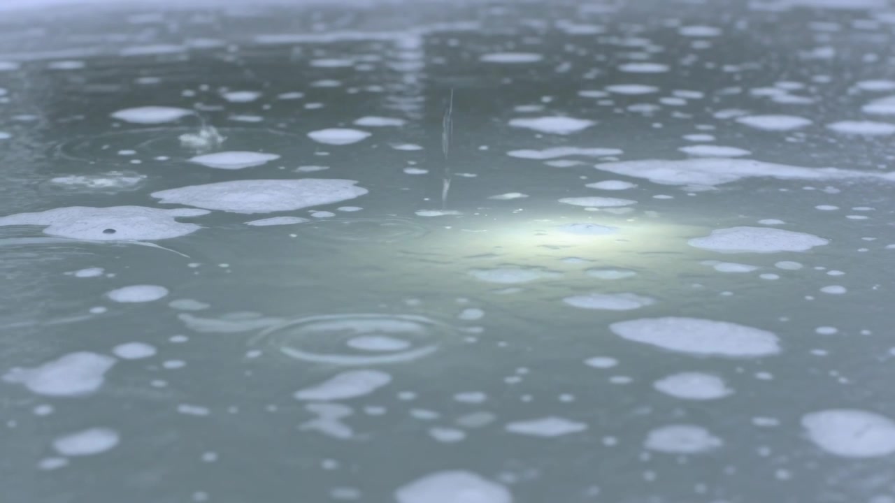 池の下で揺らめく緑色の光が動き、小雨が泡の塊とかすかな杭の間に波紋を作っている。