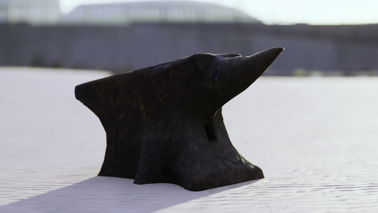 Unique black anvil resting on sunlit sandy shore at midday