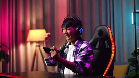 excited asian teen boy gamer celebrates victory while playing video game on smartphone