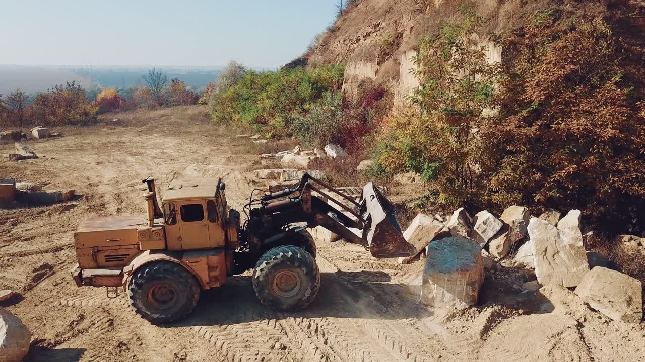 specially machinery with a bucket for picking stones is working in a quarry near the hill with forest. Close-up