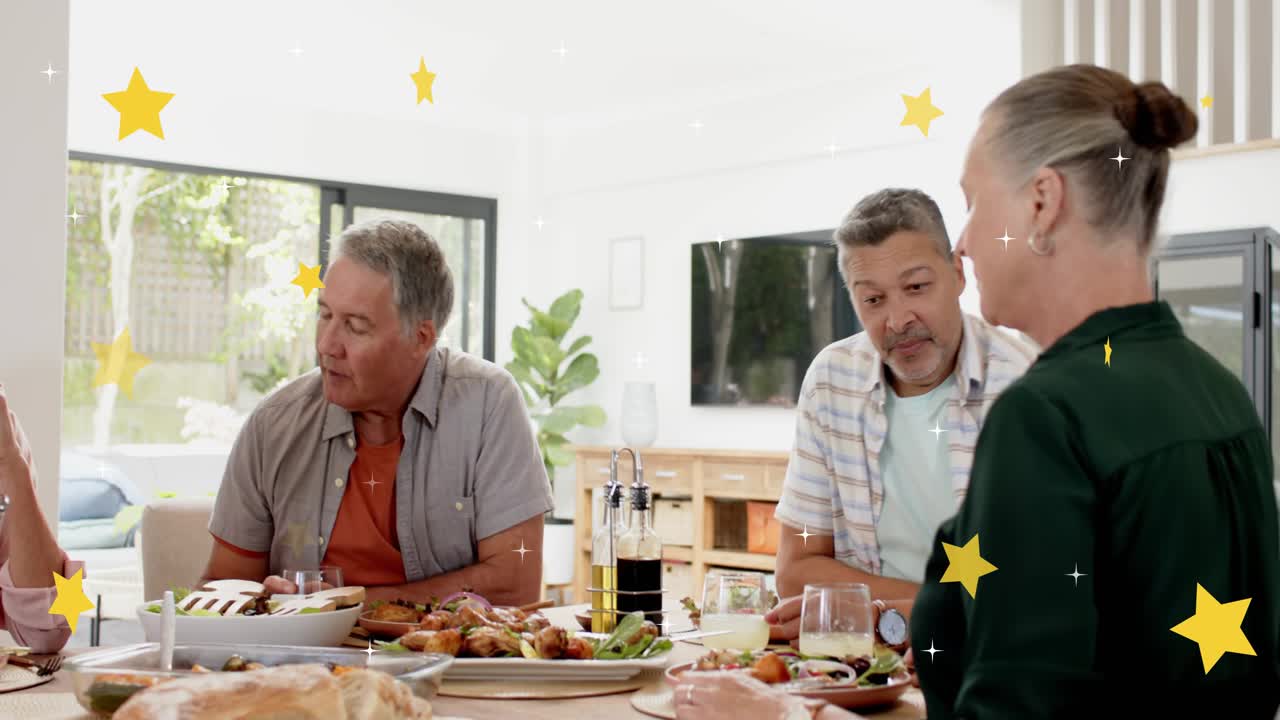 Central man speaking and lifting glass at table, leading toast while yellow stars overlaying meal