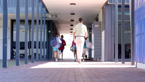 in a school corridor, a caucasian male teacher leads a diverse group of students