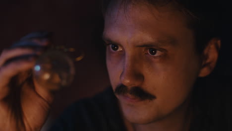 man with mustache intently examines a glass sphere