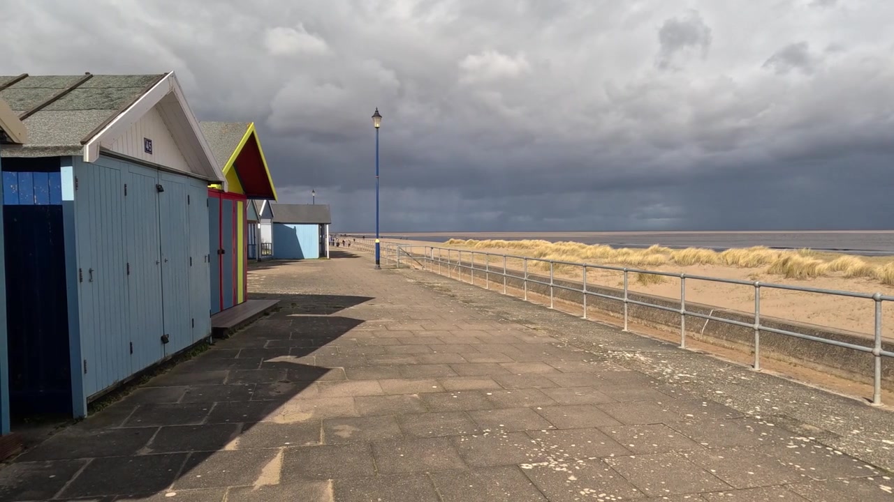 Colorful beach huts stood in a line along the seafront with sandy beach and moody grey sky’s. UK