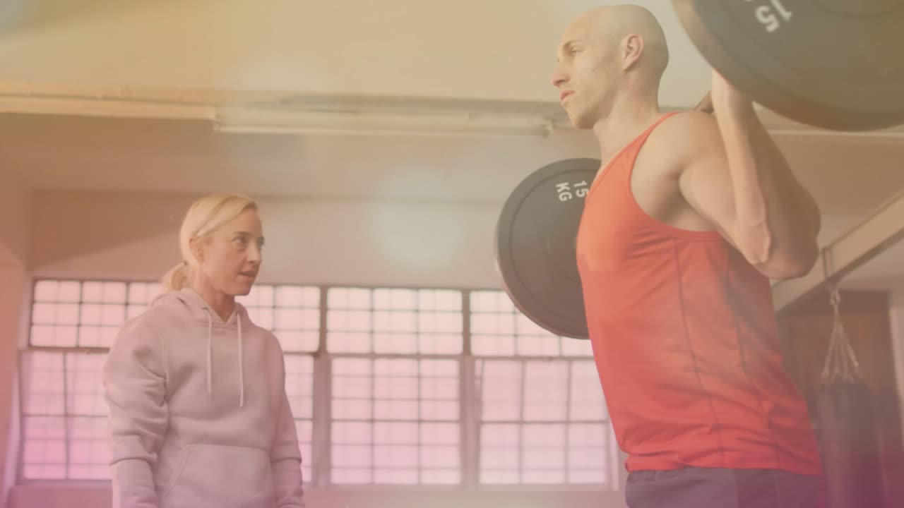 Fitness trainer stepping in, checking squatting client with barbell, giving hip cues fixing form