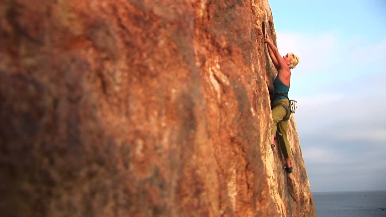 panright de un escalador que intenta escalar la pared de un acantilado sobre el océano pacífico
