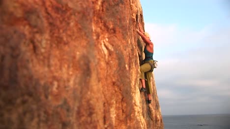 panright of a rock climber attempting to climb a cliff wall over the pacific ocean