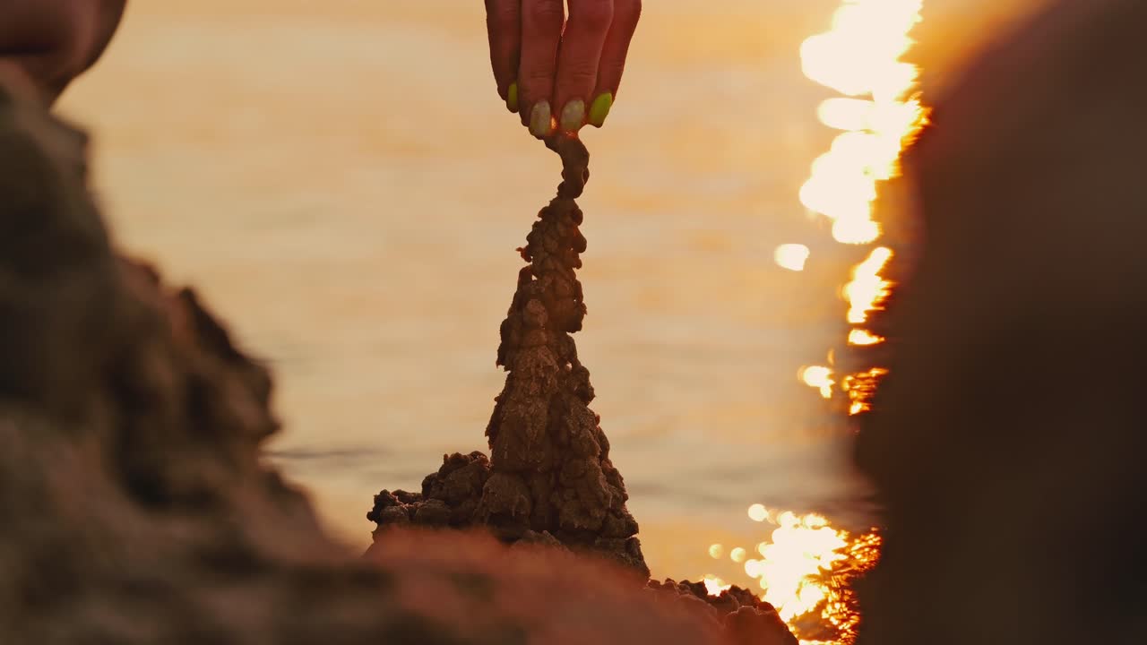 Gentle hand sculpts fragile sand tower while warm Baltic sunset light fades