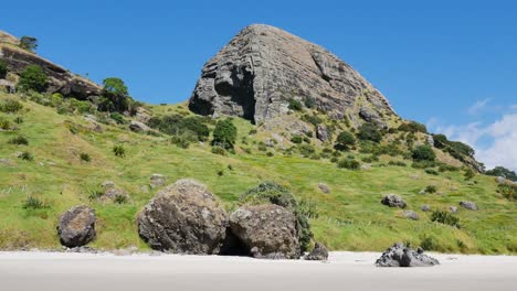 toma panorámica de una gran montaña con pradera verde y playa de arena vacía durante un hermoso día soleado con cielo azul en la bahía de los espíritus, nueva zelanda