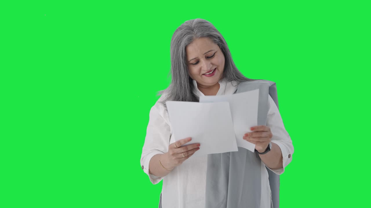 Happy Indian senior female manager reading business reports Green screen
