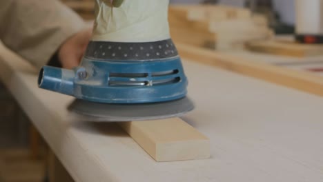 a female carpenter works with a sander on a wooden block in a workshop. close-up