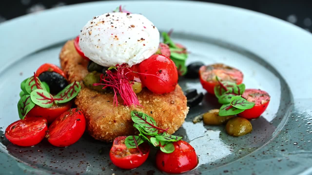 Tasty dish with fried food, fresh tomatoes, and herbs on a blue plate. A plate holds a fried piece of food topped with fresh tomatoes and herbs, served with creamy sauce