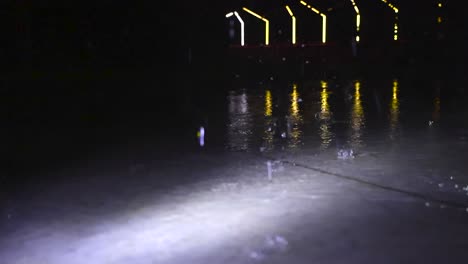 low angle video of heavy and large raindrops falling on a gray concrete floot outdoors in the night time in slow motion, with water splatter and splashing. design led lights at bokeh dark background