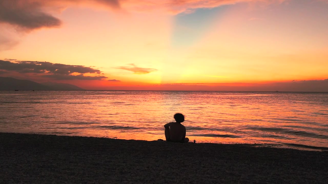 Persona seduta da sola sulla spiaggia che guarda un tramonto tropicale nelle Filippine.