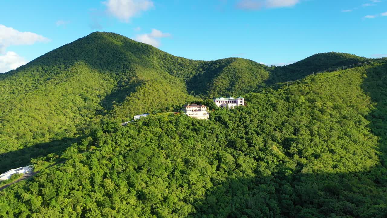 Drone footage of inland St. Croix captures luxurious homes nestled in forested terrain, surrounded by curving hills and green island mountains glowing softly in the Caribbean daylight overhead