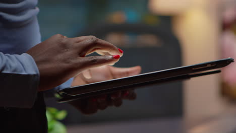 African-employee-using-tablet-standing-in-living-room-late