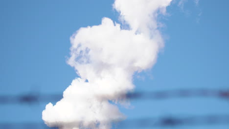 chimenea de humo en la parte superior de la fábrica en el otro lado de la valla de alambre de púas