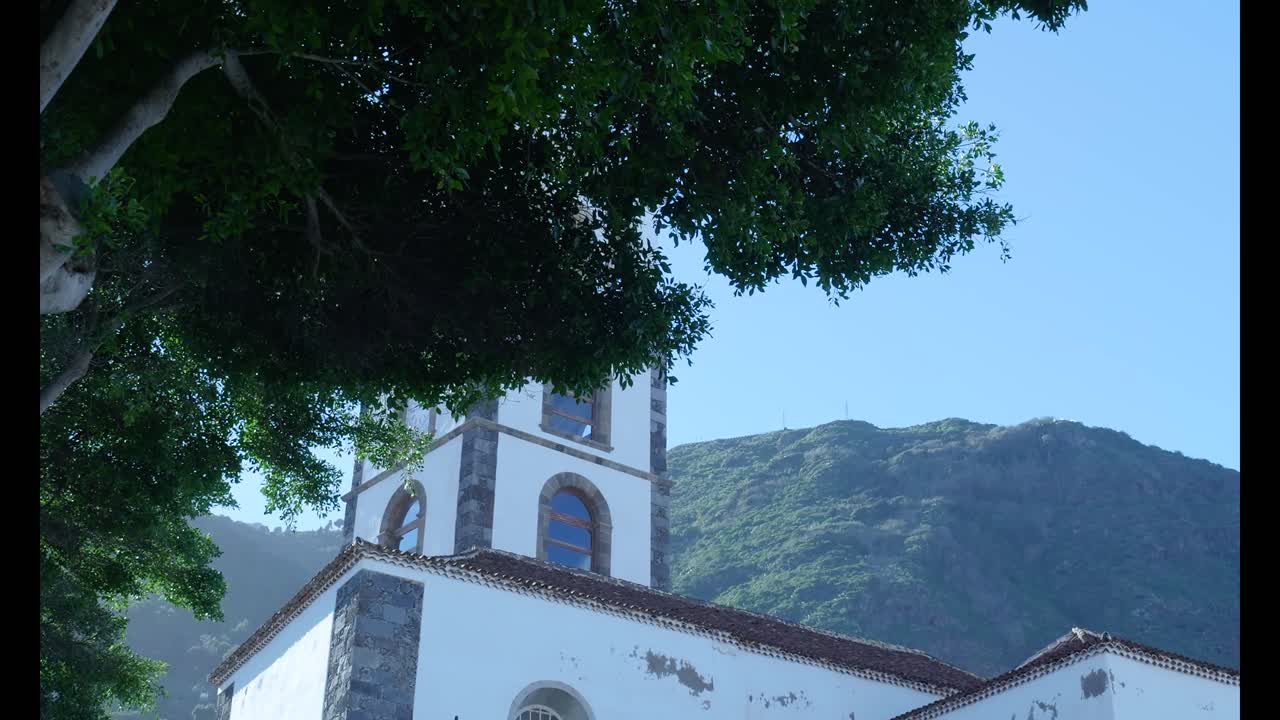 Campanile storico della chiesa bianca con sfondo montuoso a Garachico