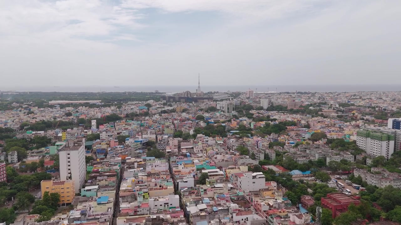 Tetti colorati affollano la vecchia Chennai mentre un drone avanza verso una costa marina nebbiosa