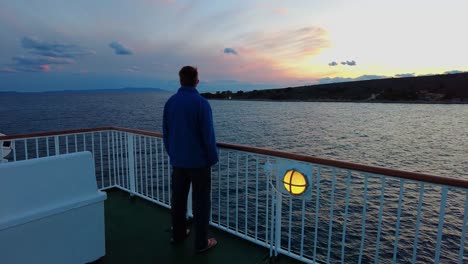 panning back view of a man standing on the edge of the dock of ferry boat looking into the distance at clouds