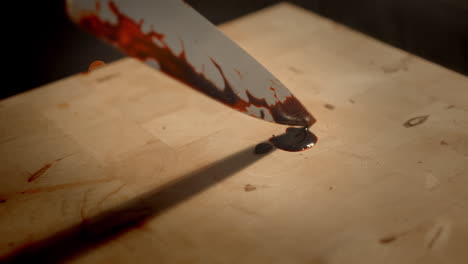 bloody big knife falls down on a wooden plate in a shady low lit room