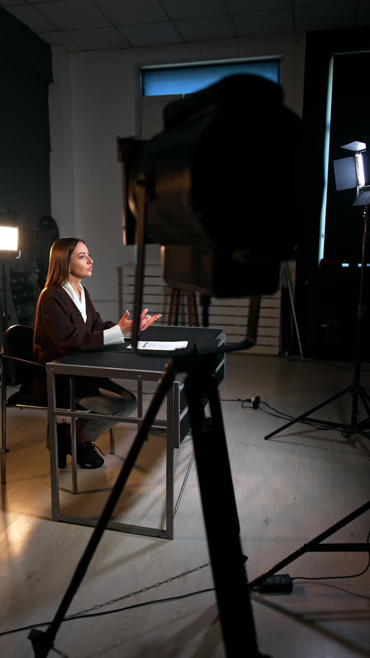 Studio footage of a blog. Brunette woman sitting at desk speaks to camera. Soffits around the blogger. Vertical video.